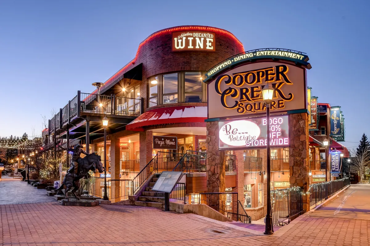 The lively Cooper Creek Square sign welcomes visitors to a vibrant area bustling with decorative lighting, boutique shops, and social spaces, reflecting the year-round vibrancy of downtown Winter Park.
