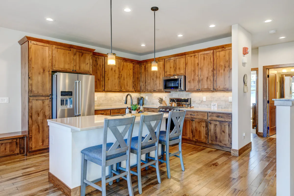 A spacious, modern kitchen featuring a large kitchen island with wooden cabinets and sleek stainless steel appliances. Bar stools are neatly arranged at the island, inviting casual gatherings and conversation. The setting is lively, perfect for entertaining or enjoying family meals.
