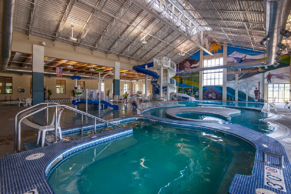 A bustling indoor recreation center with water slides, swimming pools, cheerful murals, and children actively playing, illustrating lively family activities.