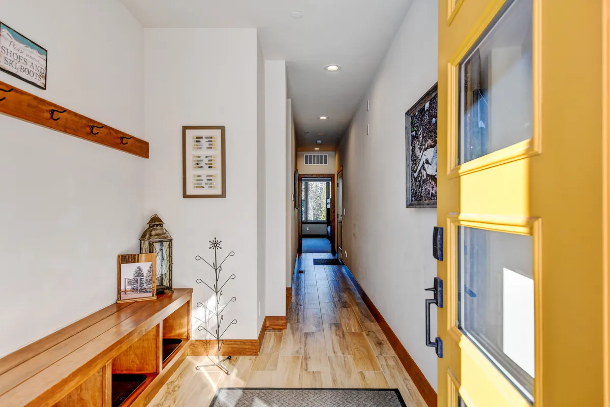 This image shows a bright yellow front door, a wooden bench with storage, decorative lanterns, and welcoming wall art. The entryway is cheerful and organized, creating a sense of arrival and homecoming.