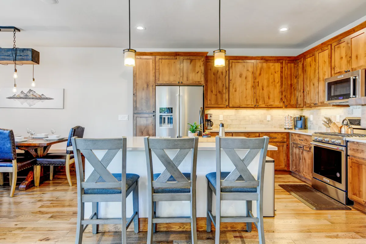A cozy, inviting kitchen area with a spacious island, wooden cabinetry, a breakfast bar with stools, and a nearby dining table. The space is well-lit and exudes warmth, making it ideal for both meal preparation and gatherings with family or friends.