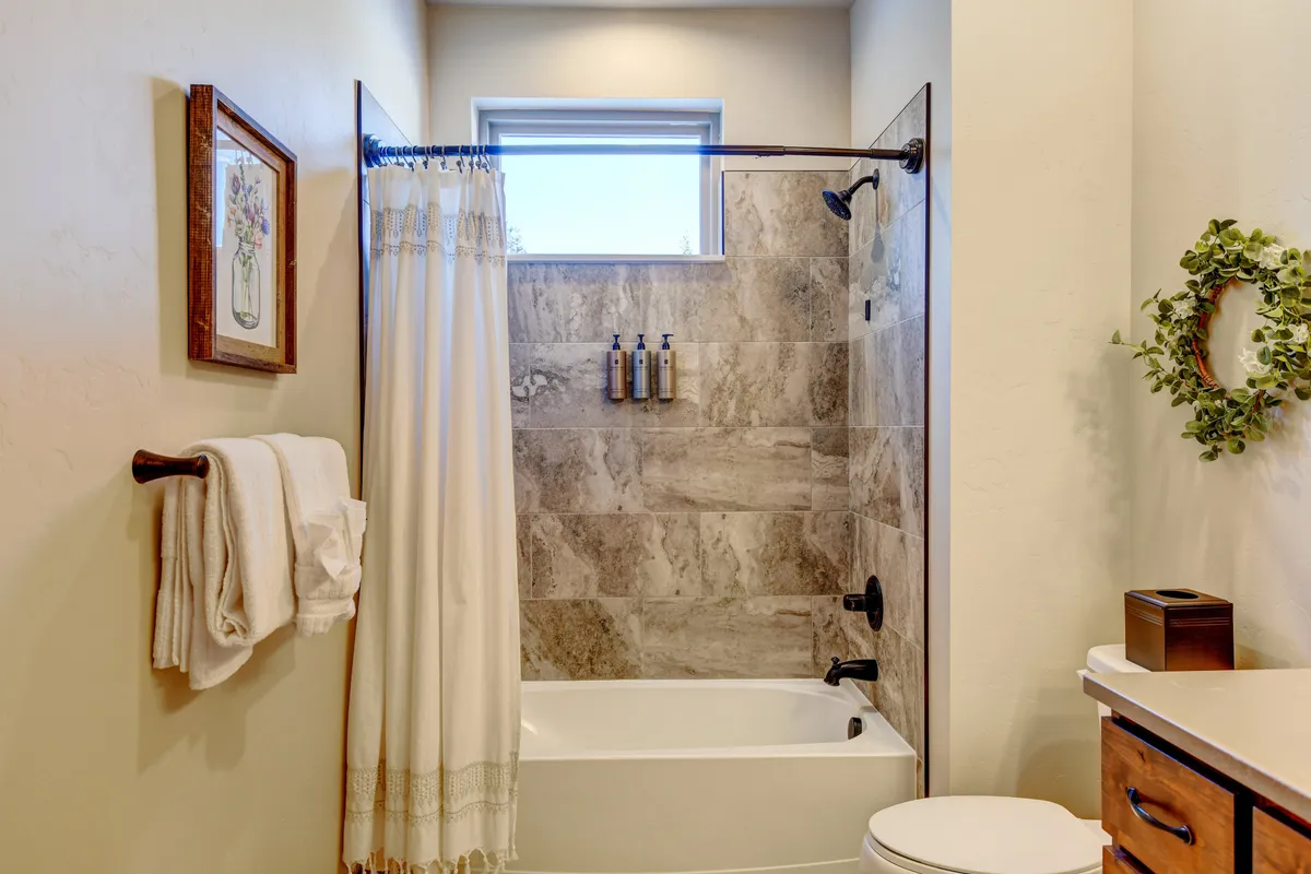 A spa-inspired bathroom with a spacious bathtub, modern shower area, vintage artwork, and decorative wreath. The space is styled with thoughtful details, creating an inviting and calming environment for post-adventure self-care and relaxation.