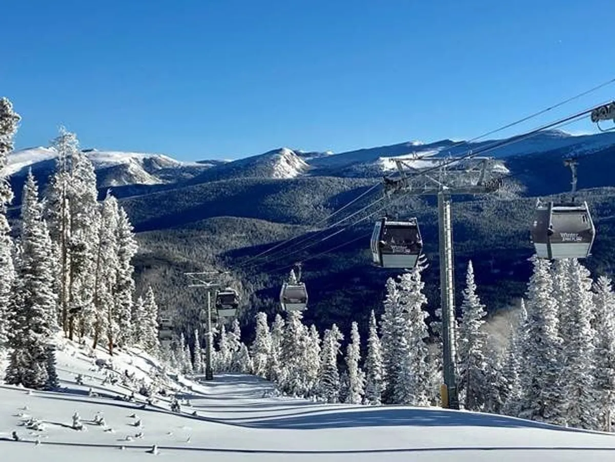 A breathtaking view of gondolas gliding above snow-covered trees with a dramatic mountain range in the background, evoking the excitement of winter sports and alpine adventure.