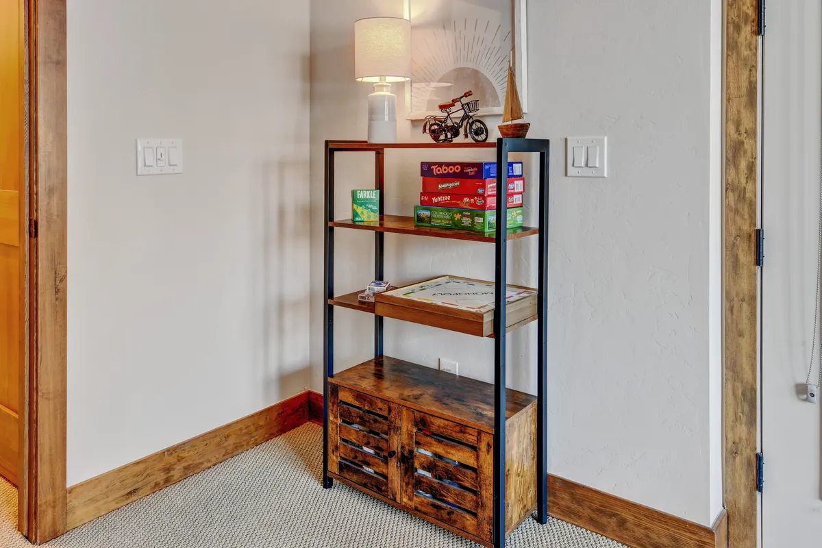 A cozy interior corner with a shelf filled with board games, a decorative lamp, and a wooden storage unit adorned with playful figurines. The setting suggests relaxed social gatherings and fun-filled game nights for all ages.