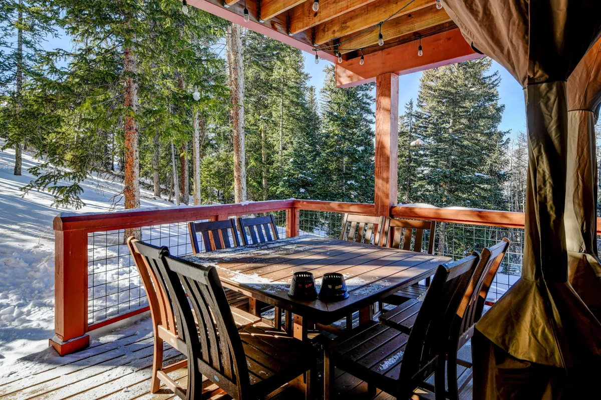 This exterior scene features a wooden dining table and chairs set on a snow-covered ground, embraced by tall trees. The atmosphere is peaceful and cozy, ideal for outdoor gatherings or simply enjoying the natural surroundings.