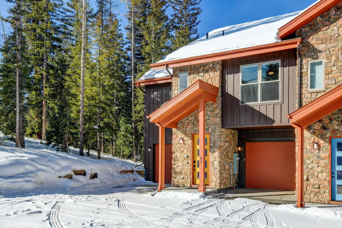 A welcoming exterior view of the property with a stone facade, warm orange accents, and a snow-covered landscape, suggesting the coziness and accessibility of the home for families.