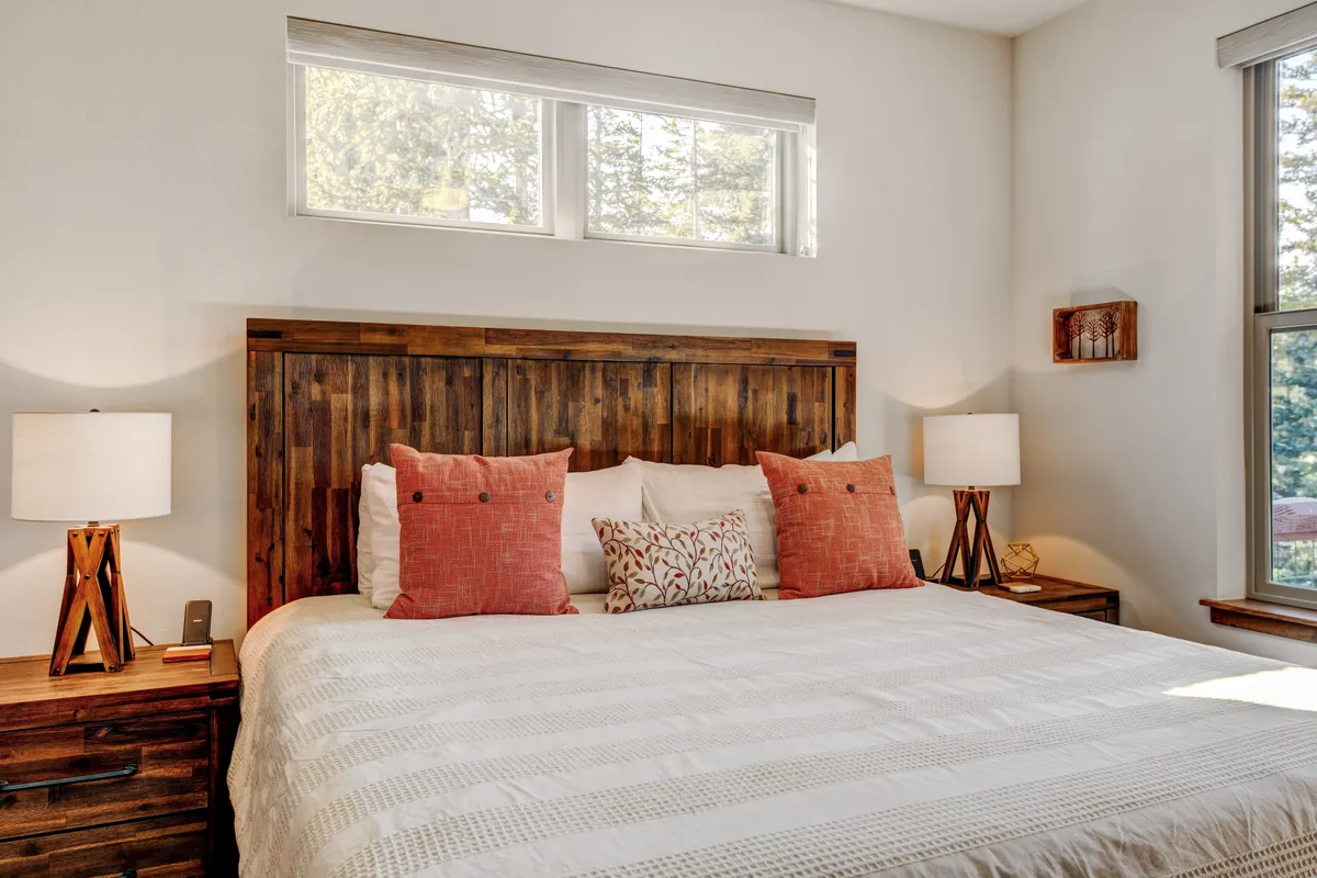 A tranquil bedroom scene with a bed featuring a wooden headboard, decorative pillows, and matching nightstands with lamps. The soft natural light streaming in and calm décor invite restful sleep and peaceful mornings.